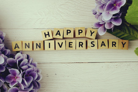 Happy Anniversary alphabet letters with flowers bouquet on wooden backgroundの写真素材