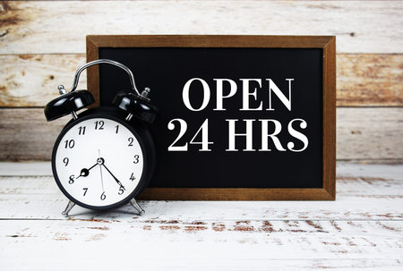 Open 24 HRS text message with alarm clock on wooden background