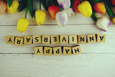 Happy Anniversary alphabet letters with flowers bouquet on wooden backgroundの写真素材