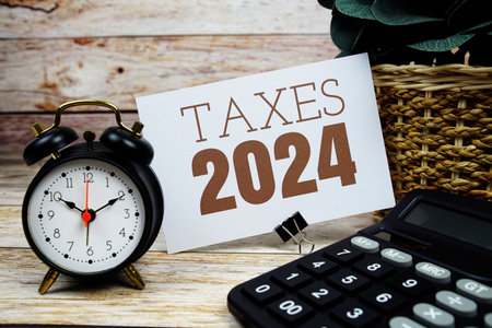 Taxes 2024 text with alarm clock and calculator on wooden backgroundの写真素材