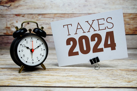 Taxes 2024 text with alarm clock on wooden backgroundの写真素材