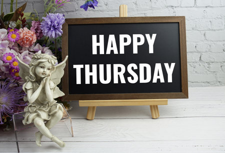 Happy Thursday text with flowers and ceramic doll decoration on white brick wall and wooden backgroundの写真素材