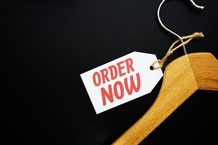 Order Now on price tag with wooden clothes hanger top view on black background