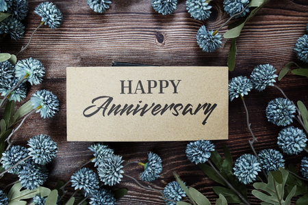 Happy Anniversary text message on paper card with flowers border frame on wooden backgroundの写真素材