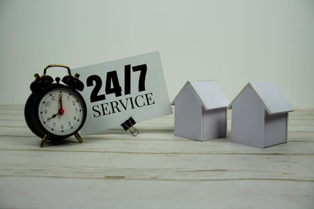 24hrs And 7 Day Service text message with alarm clock and white house model on wooden background