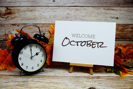Welcome October text with alarm clock and maple leaf decoration on wooden background