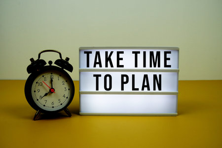Take Time To Plan text on LED light box with alarm clock on yellow background