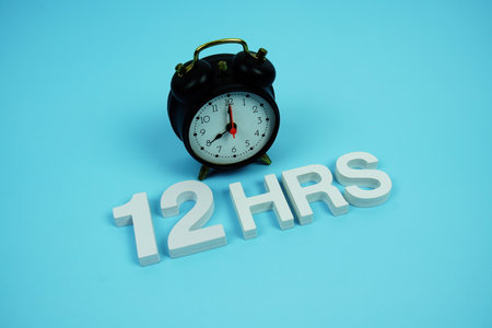 12 Hrs alphabet letters and alarm clock top view on blue backgroundの写真素材