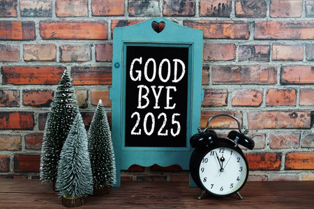 Goodbye 2025 text on blackboard easel stand with alarm clock on wooden and old brick wall background