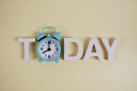Today alphabet letters with alarm clock on light yellow backgroundの写真素材