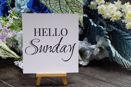 Hello Sunday text write on paper card with wooden easel and flowers decoration on wooden backgroundの写真素材