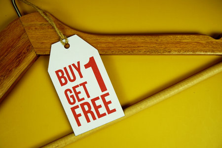 Buy 1 Get 1 Free on price tag with wooden clothes hanger top view on yellow backgroundの写真素材
