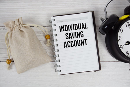 Individual Saving Account text on notepad with money bag and alarm clock on wooden backgroundの写真素材