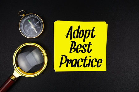 Adopt Best Practice text on sticky note with compass and magnifying glass on black backgroundの写真素材