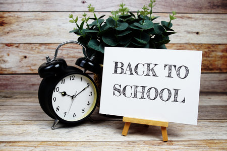 Back to School text on paper card with easel and alarm clock on wooden background, Education concept