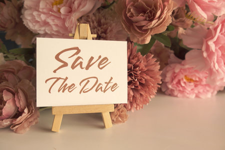 Save the date text write on paper card with wooden easel and flowers decoration on wooden backgroundの写真素材