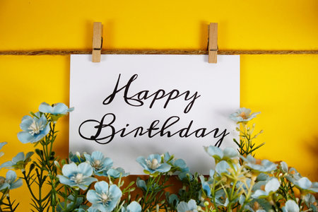 Happy Birthday text on paper card with flower blooming decoration on yellow backgroundの写真素材