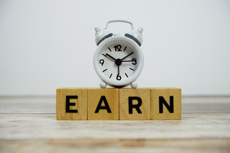 Time to Earn with wooden blocks alphabet letters and alarm clock on wooden backgroundの写真素材