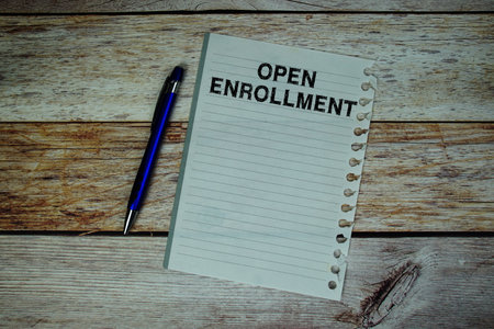 Open Enrollment text written on paper with pen and magnifying glass flat lay on wooden backgroundの写真素材