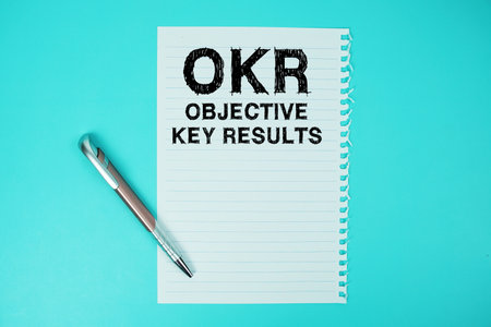OKR Objective Key Results text written on paper with pen flat lay on blue backgroundの写真素材