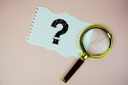 Question Mark text written on paper with magnifying glass flat lay on pink backgroundの写真素材