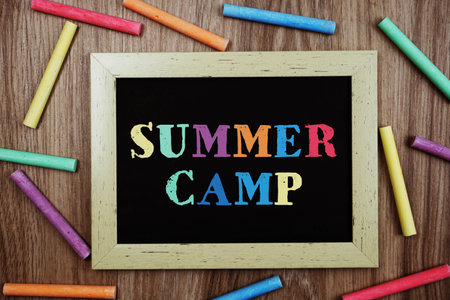 Summer Camp text on blackboard with chalk stick various colors on wooden backgroundの写真素材