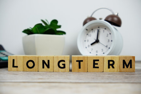 Alarm clock with wooden blocks alphabet letters LONG TERM text message on wooden backgroundの写真素材