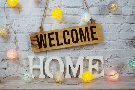 Welcome Home alphabet letters and wooden signboard hanging on white brick wall background