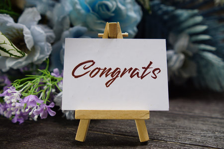 Congrats text write on paper card with wooden easel and flowers decoration on wooden backgroundの写真素材