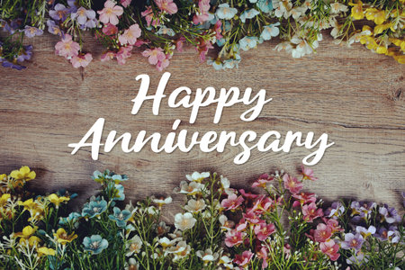 Happy Anniversary text message with flowers decoration on wooden backgroundの写真素材