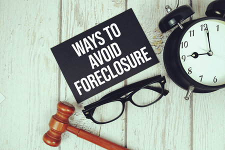 Ways To Avoid Foreclosure text on paper card with alarm clock and wooden judge gavel top view on...