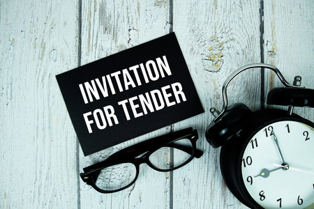 Invitation For Tender text on paper card with alarm clock on wooden background