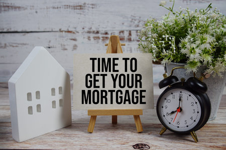 Time to Get Your Mortgage on paper card with alarm clock and white house model on wooden background