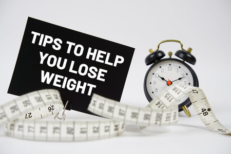 Tips To Help You Lose Weight text with alarm clock and measuring tape on white backgroundの写真素材