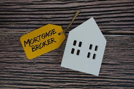 Mortgage Broker text on price tag with white house model flat lay on wooden background