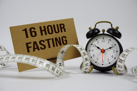 16 Hour Fasting text with alarm clock and measure tape on white backgroundの写真素材