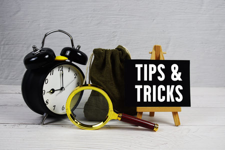 Money Savings Tips And Tricks text with alarm clock and magnifying glass on wooden background