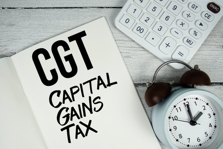 CGT Capital Gains Tax text on paper notebook page with alarm clock and calculator on wooden backgroundの写真素材