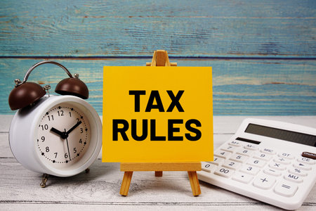 Tax Rules text written on paper card with calculator and alarm clock on wooden background
