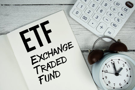 ETF Exchange Traded Fund text on paper notebook page with alarm clock and calculator on wooden...