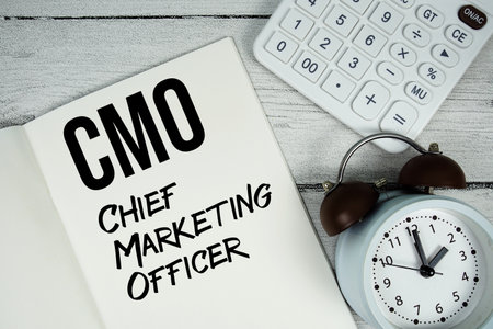 CMO Chief Marketing Officer text on paper notebook page with alarm clock and calculator on wooden backgroundの写真素材