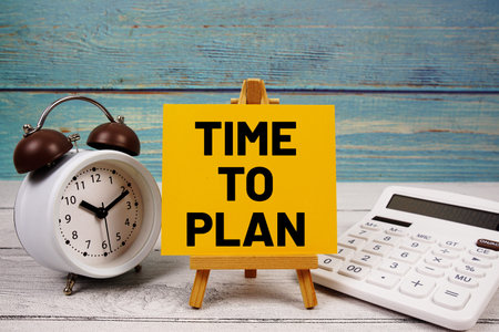 Time To Plan text written on paper card with calculator and alarm clock on wooden background