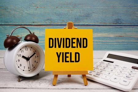 Dividend Yield text written on paper card with calculator and alarm clock on wooden backgroundの写真素材