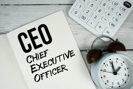 CFO Chief Executive Officer text on paper notebook page with alarm clock and calculator on wooden backgroundの写真素材