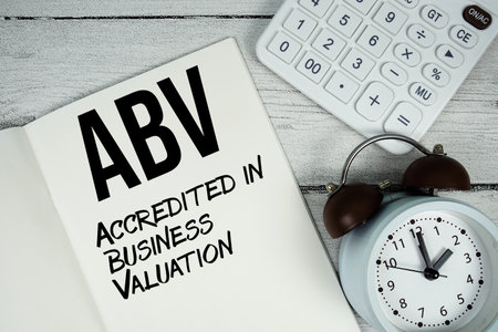 ABV Accredited in Business Valuation text on paper notebook page with alarm clock and calculator on wooden backgroundの写真素材