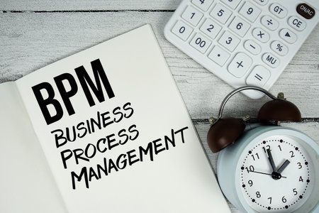 BPM Business Process Management text on paper notebook page with alarm clock and calculator on wooden backgroundの写真素材