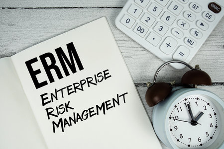 ERM Enterprise Risk Management text on paper notebook page with alarm clock and calculator on wooden backgroundの写真素材