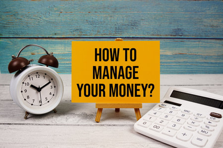 How to manage your money? text written on paper card with calculator and alarm clock on wooden backgroundの写真素材