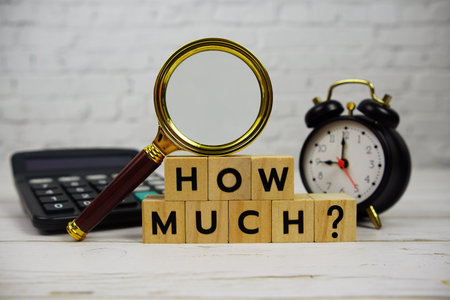 How Much? with wooden blocks alphabet letters and magnifying glass, calculator, alarm clock top view on wooden backgroundの写真素材