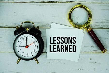 Lessons Learned text message on sticky note with magnifying glass and alarm clock on wooden backgroundの写真素材